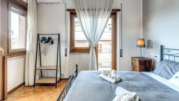 A bedroom with a bed, a bedside table with a lamp, a window with curtains, and a coat rack with hanging clothes. - Spacious Apartment Near Saint Peter's Basilica
 (Roma)