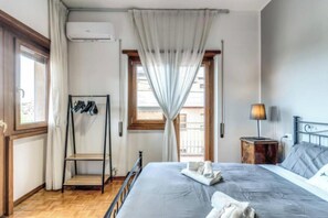 A bedroom with a bed, a bedside table with a lamp, a window with curtains, and a coat rack with hanging clothes. - Spacious Apartment Near Saint Peter's Basilica
 (Roma)