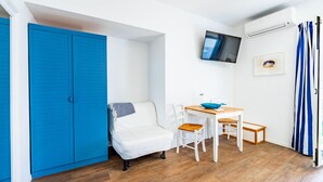 Et lille værelse med en blå garderobe, en hvid seng, et spisebord med stole og et ophængt TV.
