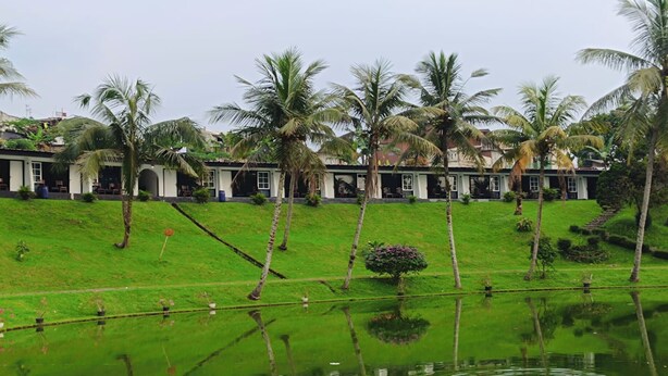 A hotel with a pool, palm trees, and a green lawn. - Capital O 94094 New Lembah nyiur (Cisarua)