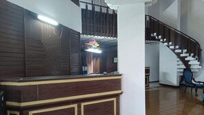 A reception area with a wooden counter, a staircase, and a hanging floral decoration. - Capital O 94094 New Lembah nyiur (Cisarua)