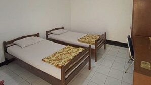 A room with two wooden beds, each with a patterned bedspread and white pillows. The room has white walls and a tiled floor. - Capital O 94094 New Lembah nyiur (Cisarua)