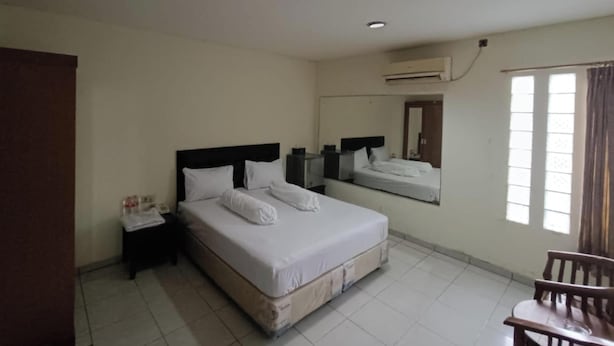 Habitació d'hotel amb dos llits, una taula petita, una cadira i una finestra amb cortines.