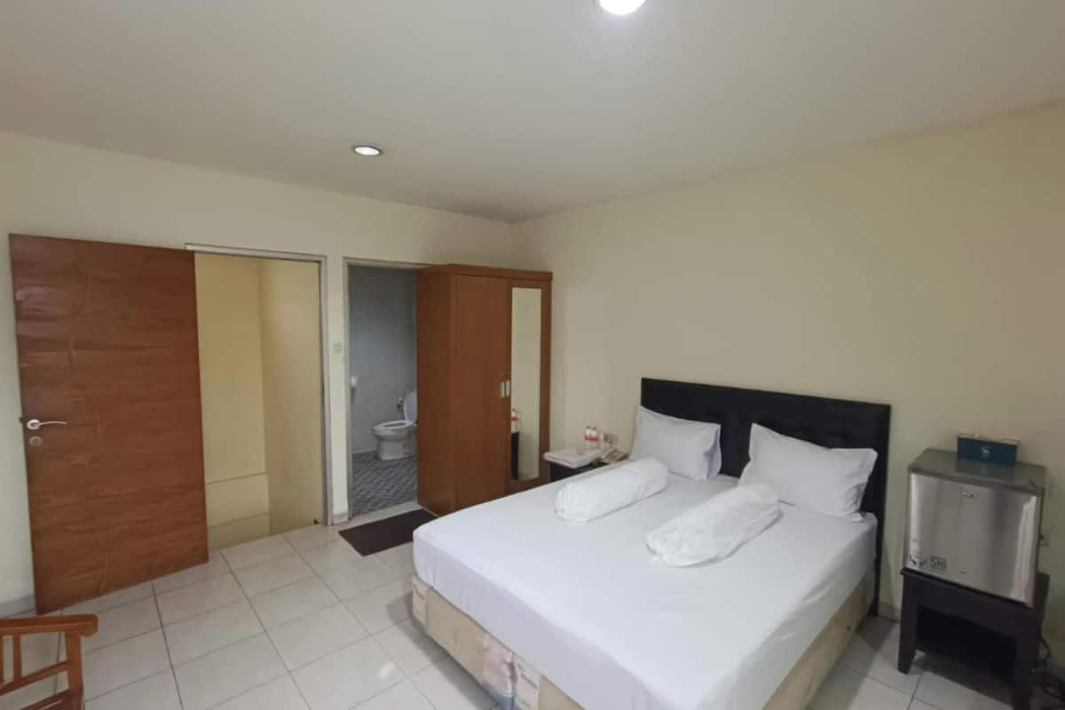 A hotel room with a bed, a nightstand, a wooden chair, and a bathroom visible through an open door.