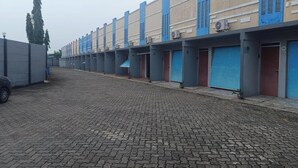 Fila d'habitacions d'hotel amb façanes blaves i beix, un pati pavimentat i un cotxe aparcat.