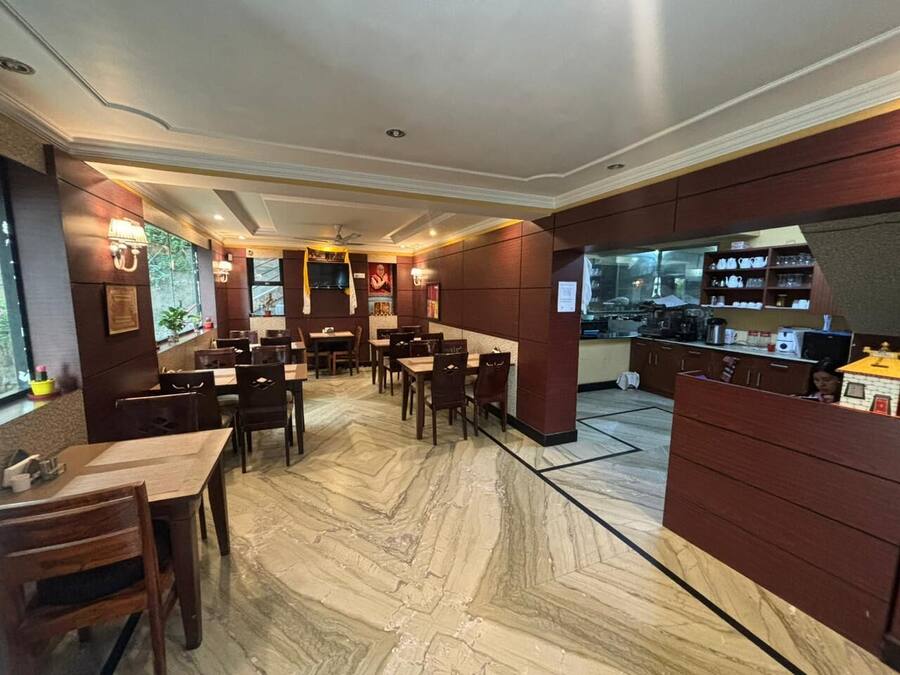 A restaurant with marble flooring, wooden tables and chairs, and a kitchen area visible through a glass partition.