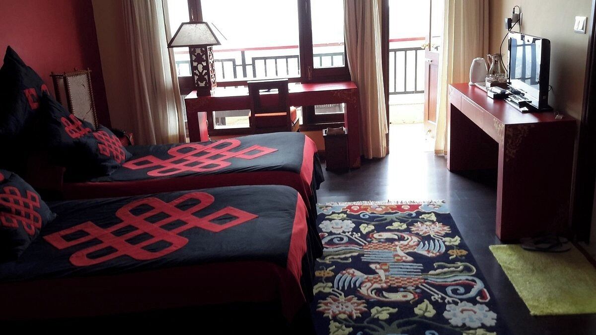 A hotel room with two beds, a desk, a TV, and a view of the outside balcony.
