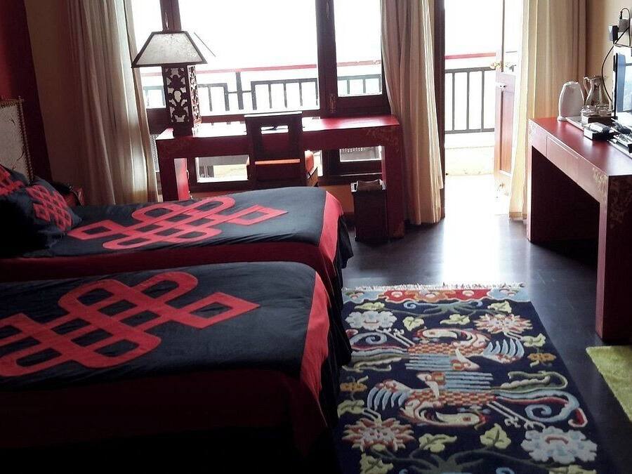 A hotel room with two beds, a desk, a TV, and a view of the outside balcony.