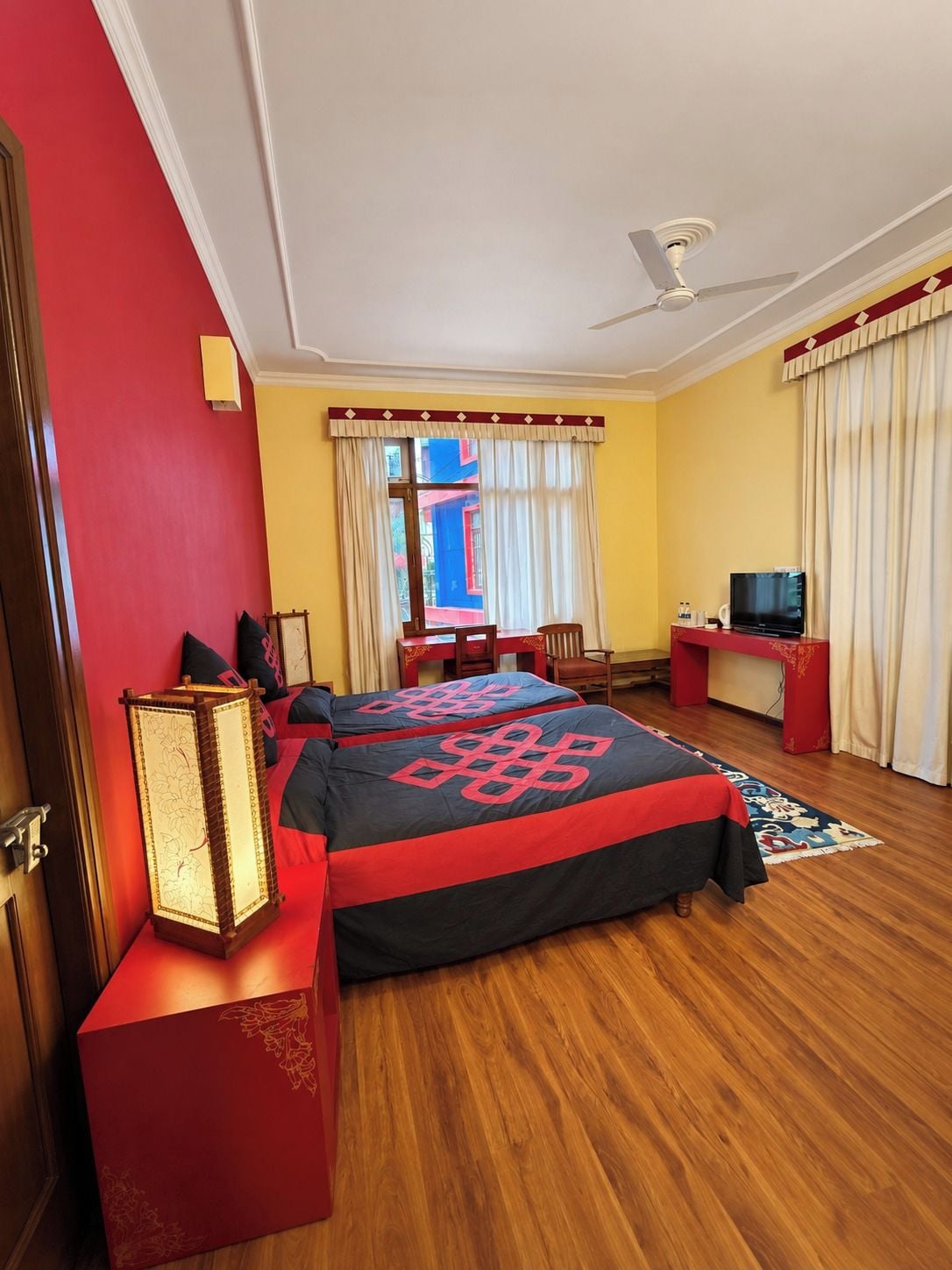Ein Hotelzimmer mit einem Bett, einem Schreibtisch, einem Fernseher und einem Fenster mit Vorhängen.