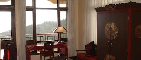 Una habitación tradicional con un mueble de madera grande, una mesa, sillas y vistas a un paisaje montañoso a través de amplios ventanales.