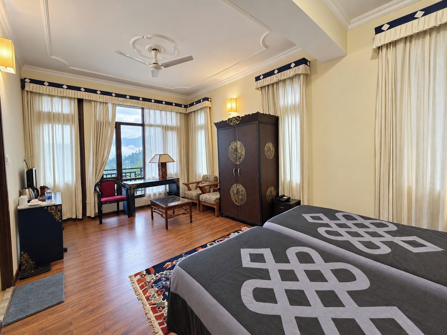 A hotel room with a bed, a desk, a chair, a wardrobe, and a view of the outdoors.