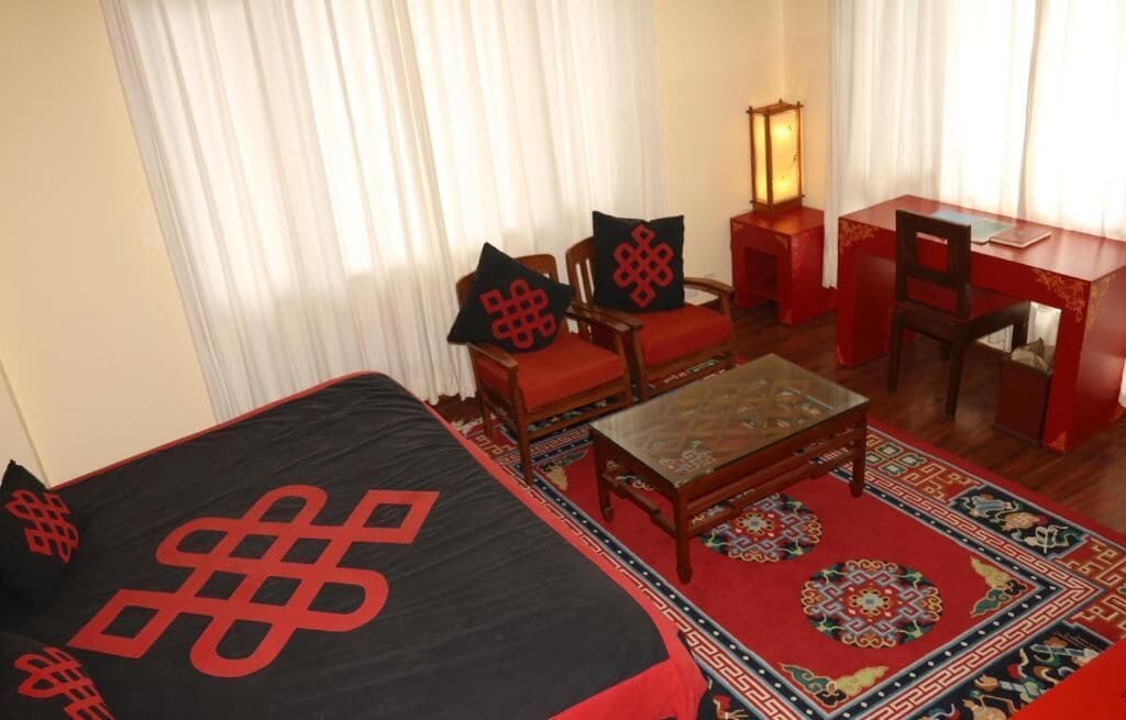 A hotel room with a bed, two chairs, a small table, a desk, and a lamp.