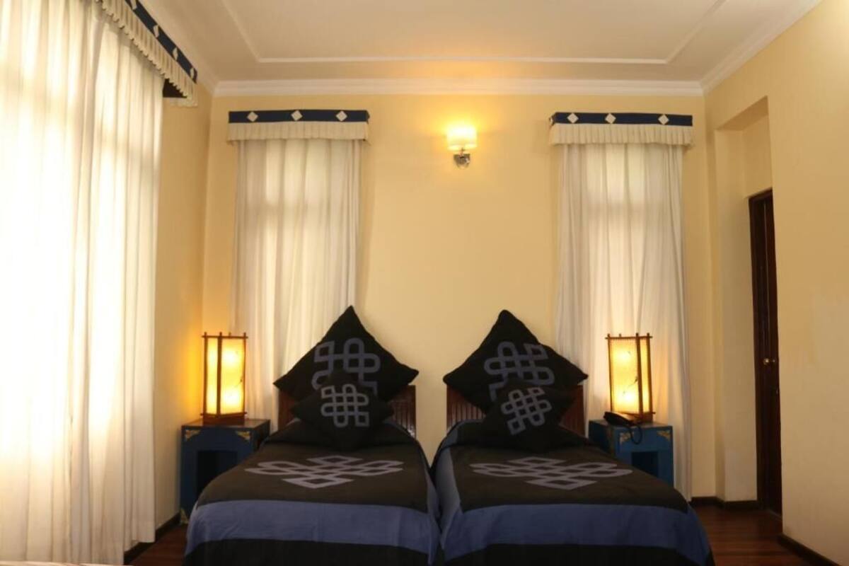 Habitación de hotel con dos camas, cada una con almohada y mesita de noche con lámpara.