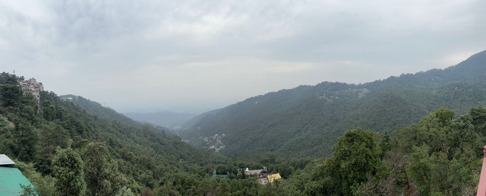 A valley with dense forest and a few buildings on the hillsides.