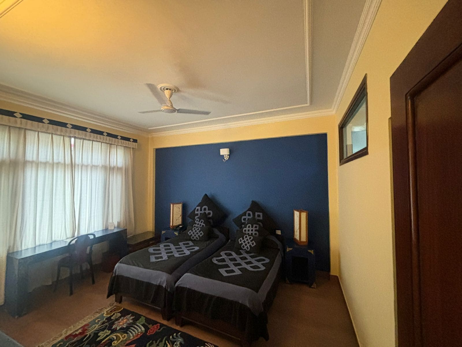 A bedroom with two beds, a ceiling fan, a desk, and a window with curtains.