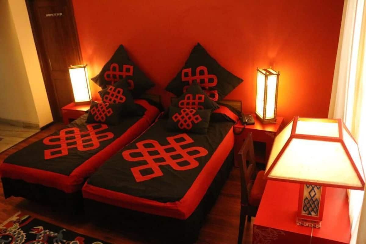 Una habitación con dos camas, cada una con una colcha negra y almohadas rojas con un estampado geométrico. Hay lámparas de noche a ambos lados de las camas.
