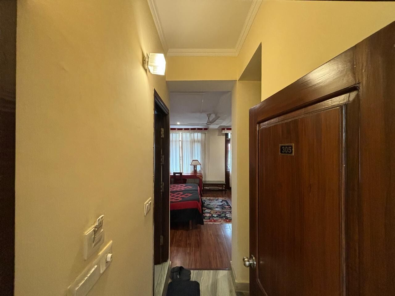 A hotel hallway leading to a room with a bed, a desk, and a chair.