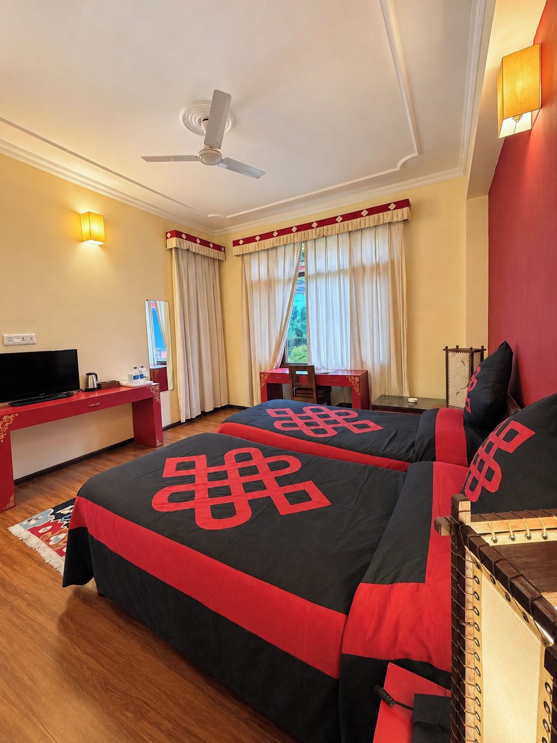 A hotel room with two beds, a desk, a television, and a ceiling fan.