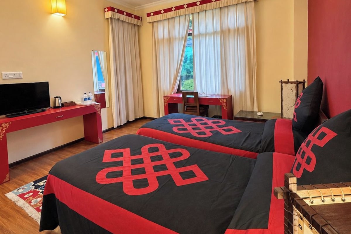 A hotel room with two beds, a desk, a television, and a ceiling fan.