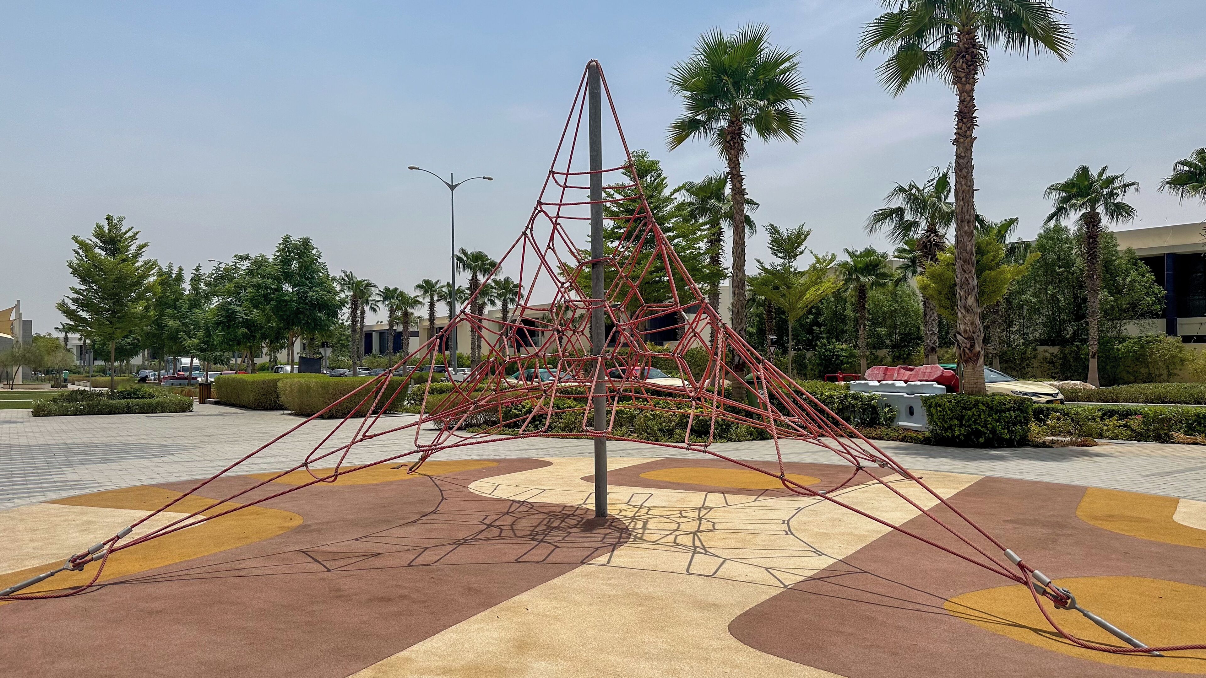 A geometric metal sculpture in a landscaped area with palm trees and a paved walkway.