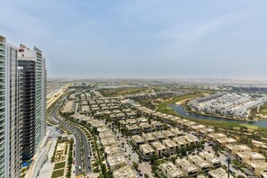 A high-rise building with a modern design, surrounded by a residential area with a river and green spaces. - Waves - Elegant 28th Floor Studio in Carson A, Damac Hills (Dubai)