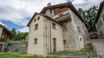 A traditional stone building with a balcony, a staircase leading to an upper level, and a small garden area in front.