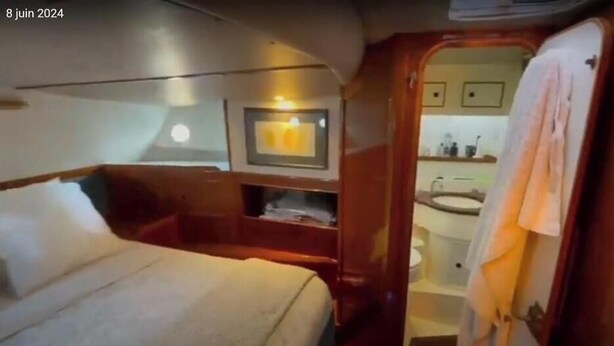 A compact cabin with a bed, a small seating area, a vanity with a mirror, and a sink. - Boat rental (Marseille)