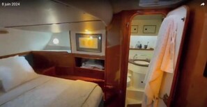 A compact cabin with a bed, a small seating area, a vanity with a mirror, and a sink. - Boat rental (Marseille)