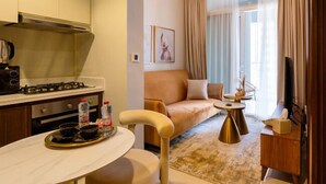 A modern kitchen with a gas stove, a dining table with chairs, a sofa, and a small side table. - Burj Khalifa View - High Floor 1BR Apt (Dubai)