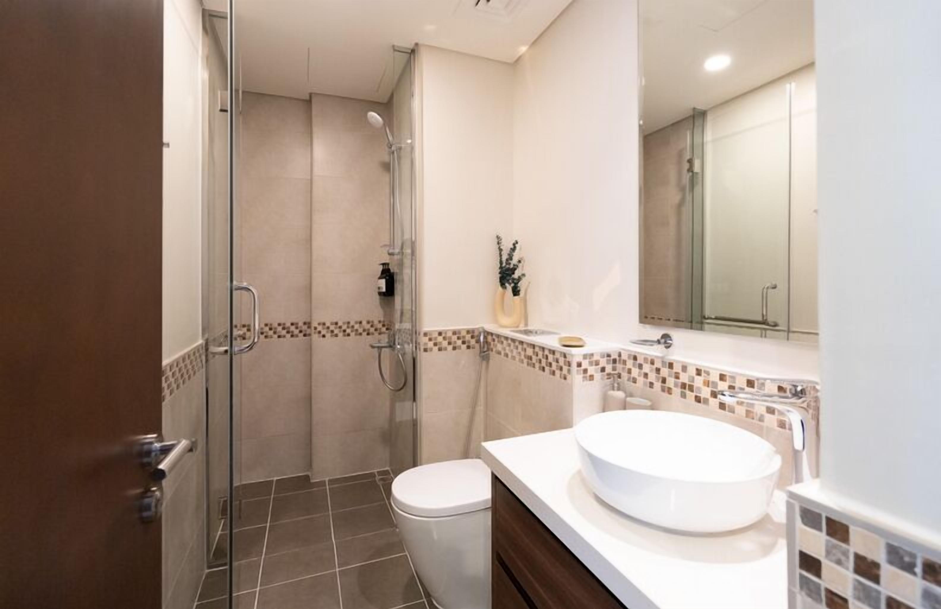 Ein modernes Badezimmer mit einer gläsernen Dusche, einer weißen Toilette und einem großen, runden Waschbecken.
