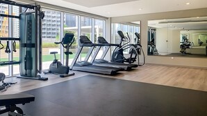 A modern gym with treadmills, a weight machine, and a bench. Large windows provide natural light and views of the city. - Burj Khalifa View - High Floor 1BR Apt (Dubai)