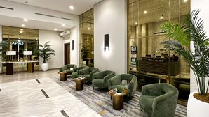 A modern lobby with green armchairs, a reception desk, and a large mirror reflecting the interior. - Burj Khalifa View - High Floor 1BR Apt (Dubai)