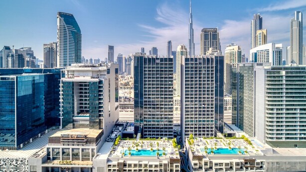A high-rise hotel with a rooftop pool area, surrounded by modern skyscrapers. - Burj Khalifa View - High Floor 1BR Apt (Dubai)