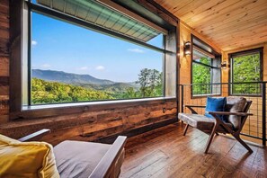 A wooden interior with a large window offering a view of a forested mountain range. - Rooftop Heated Pool - Fire Pit - Pool table - LUX (Gatlinburg)