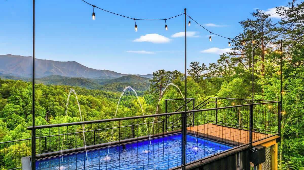 Une piscine offrant une vue sur un paysage montagneux, entourée d’arbres et d’une clôture en métal.