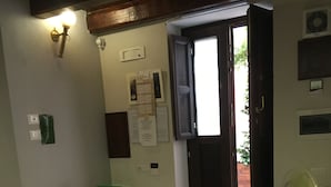 A compact living space with a kitchenette, a sofa with cushions, a chair, a fan, and a staircase leading to an outdoor area. - Ortigiadeluxe S.A.L. (Siracusa)