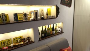 A living room with a grey sofa, colorful cushions, and shelves displaying various items including wine bottles, decorative objects, and a 'Fine Food' sign. - Ortigiadeluxe S.A.L. (Siracusa)
