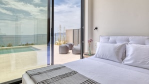 A modern bedroom with a large bed, a view of a swimming pool, and a balcony with outdoor seating. - Alpha VIlla | S Cave Villas Seaside Karystos (Karystos)