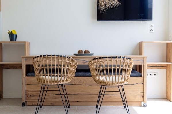 A modern room with a wooden desk, two wicker chairs, a small plant, and a flat-screen TV on the wall.