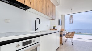 A modern kitchen with white cabinets, a black faucet, and a view of the sea through a large window. - Alpha VIlla | S Cave Villas Seaside Karystos (Karystos)