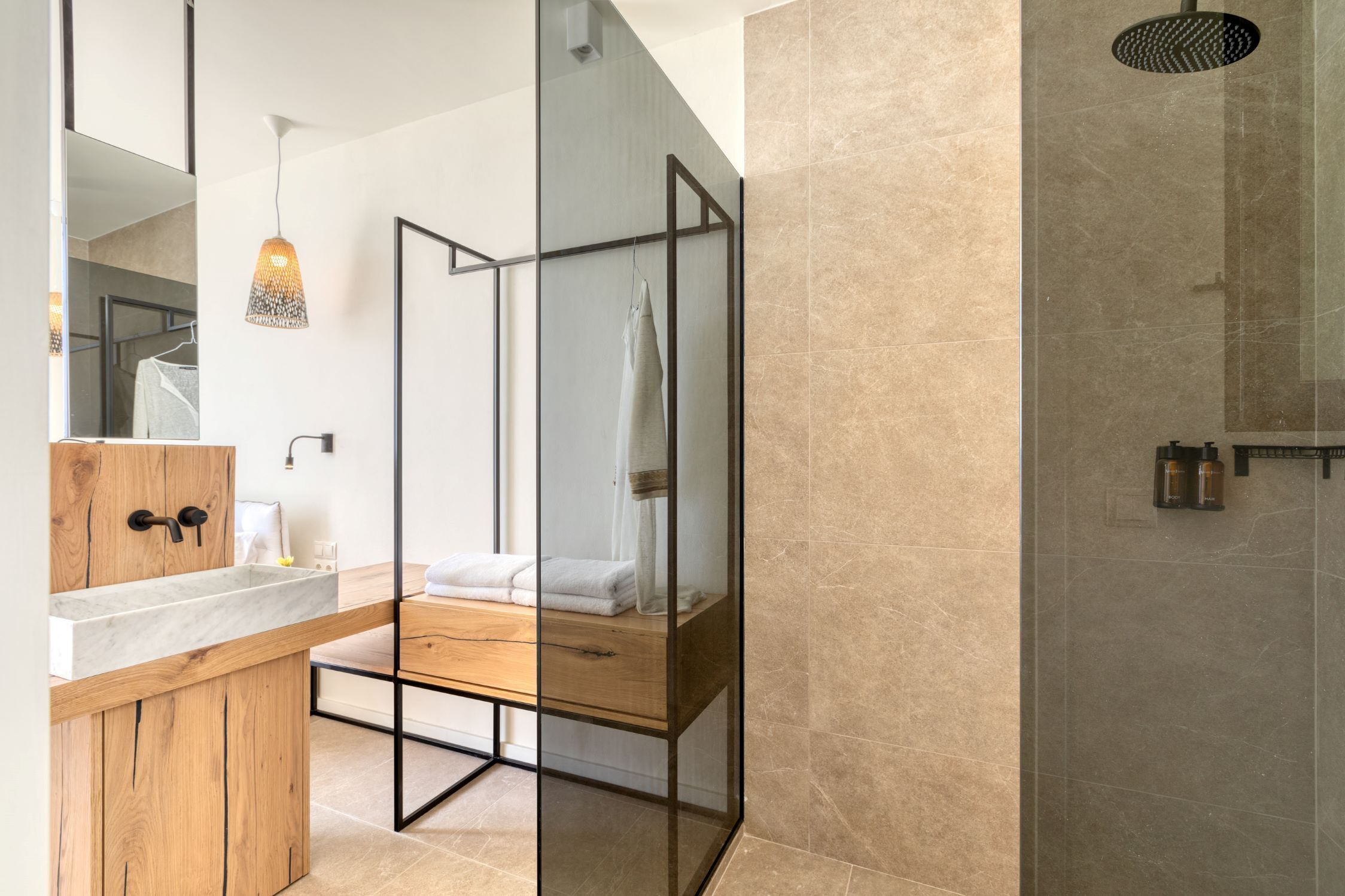 Un bagno moderno con un mobile lavabo in legno, cabina doccia in vetro e lampada a sospensione.