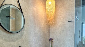 A modern bathroom with a marble sink, wooden vanity, a round mirror, a hanging light fixture, and a glass shower enclosure.