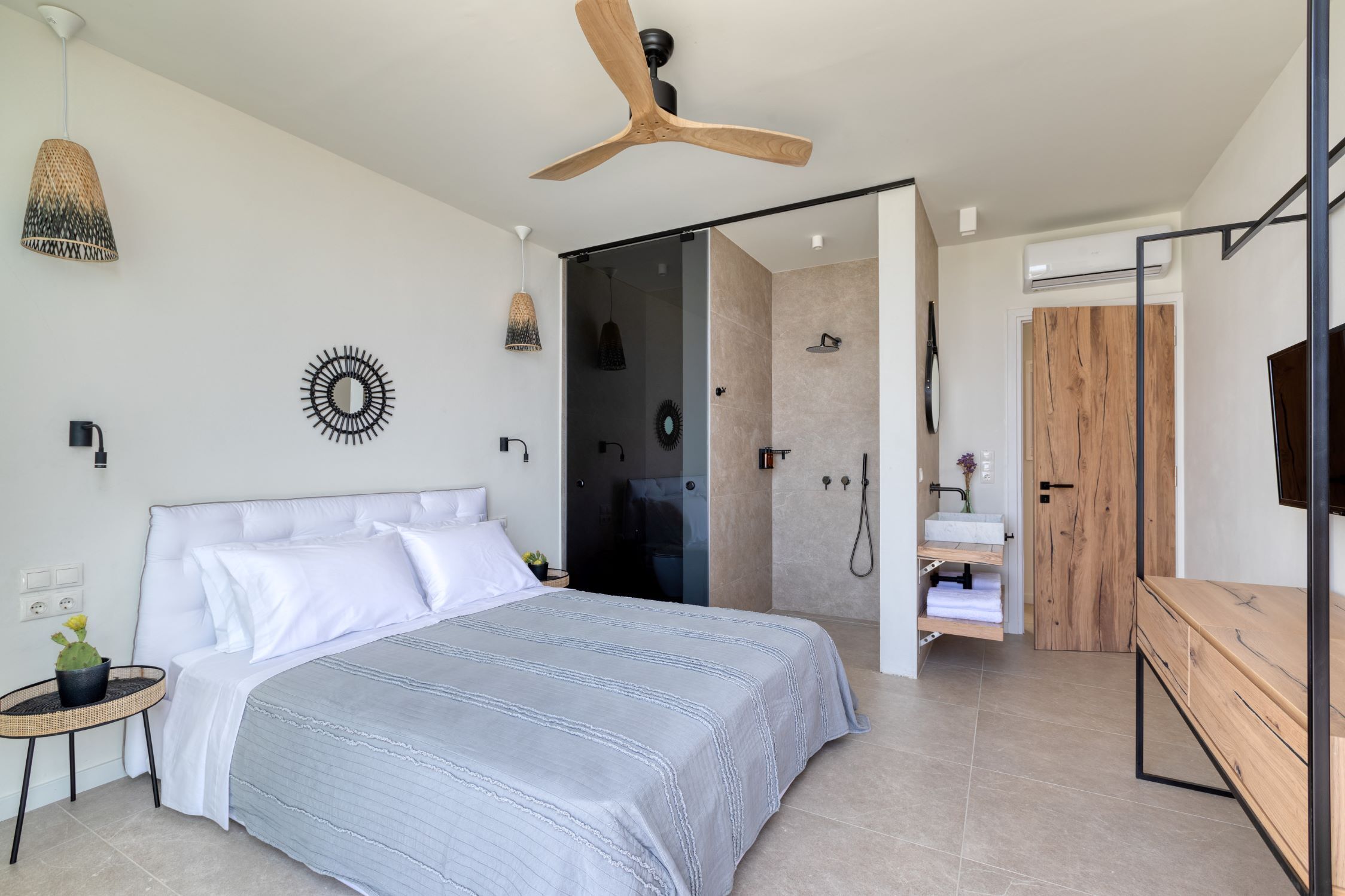 A modern bedroom with a large bed, a ceiling fan, a shower area, and a wooden vanity.