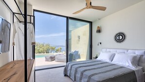 A bedroom with a large bed, a wooden desk, and a sliding glass door leading to a balcony with a pool.