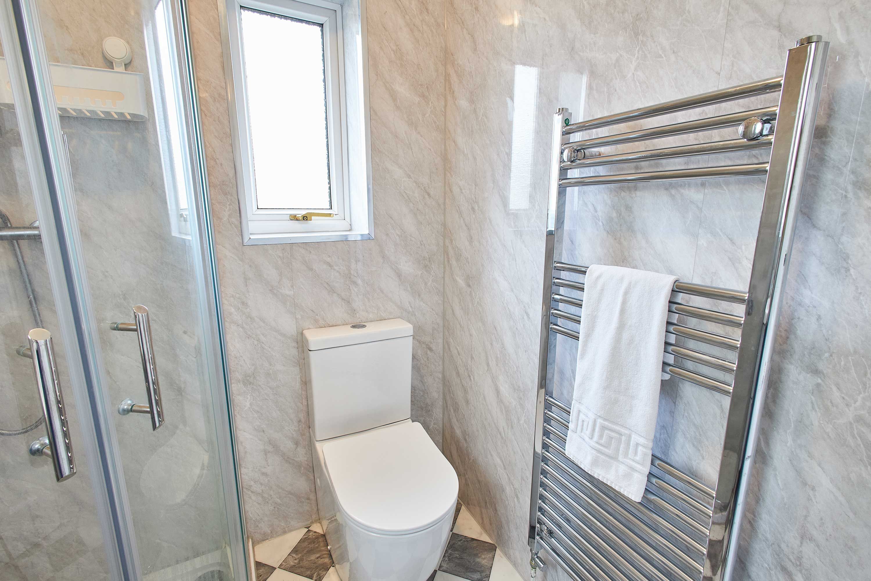 A bathroom with a glass shower enclosure, a toilet, a towel rack, and a window.