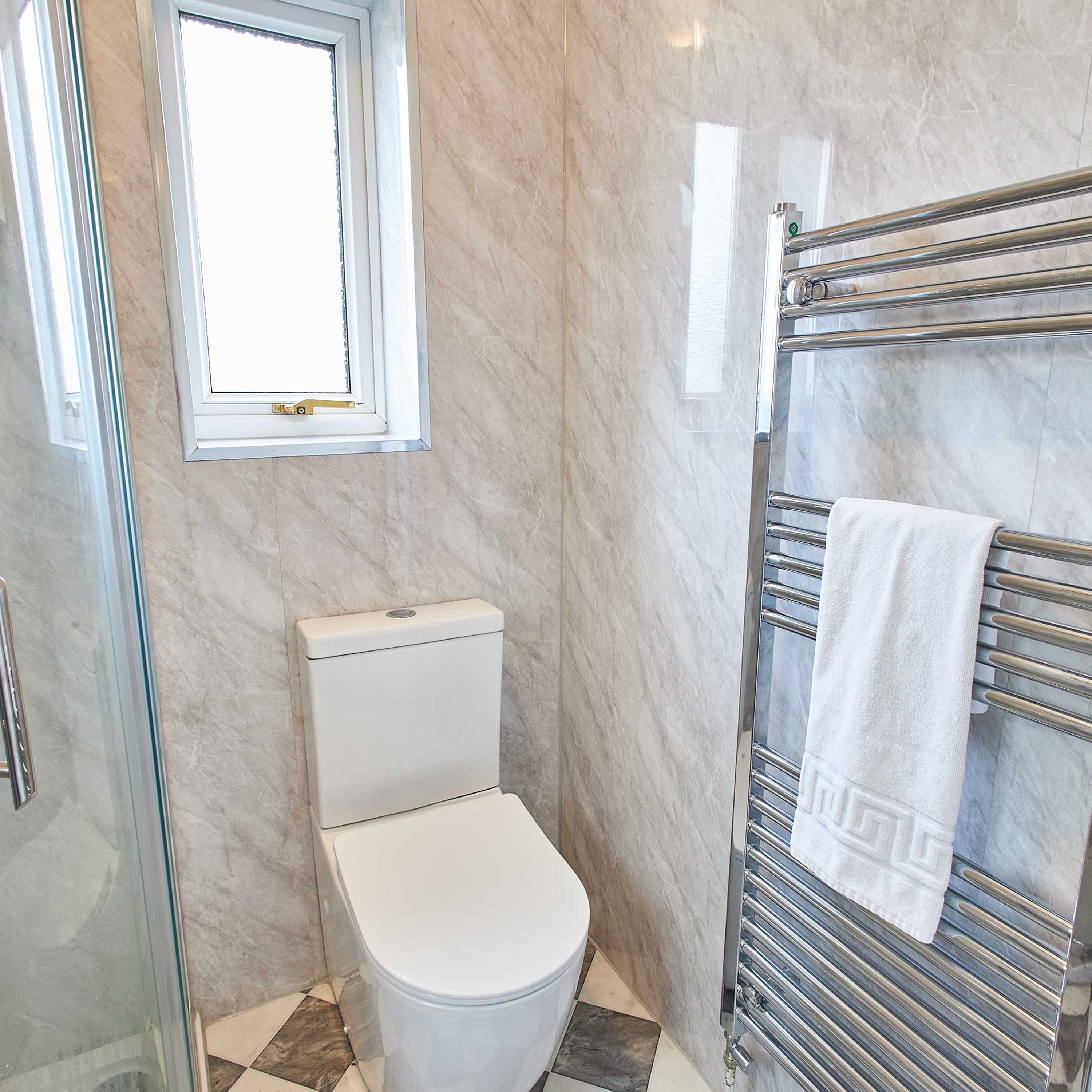 A bathroom with a toilet, a glass shower enclosure, a towel rack with a towel, and a window.