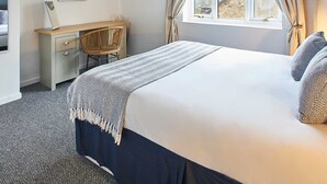 Un dormitorio con cama, escritorio, silla, un cuadro y ventana con cortinas.
