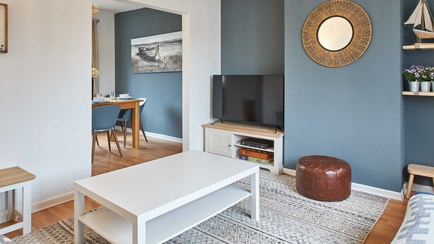 Una sala de estar moderna con una mesa de centro blanca, un televisor y un espejo grande en la pared.