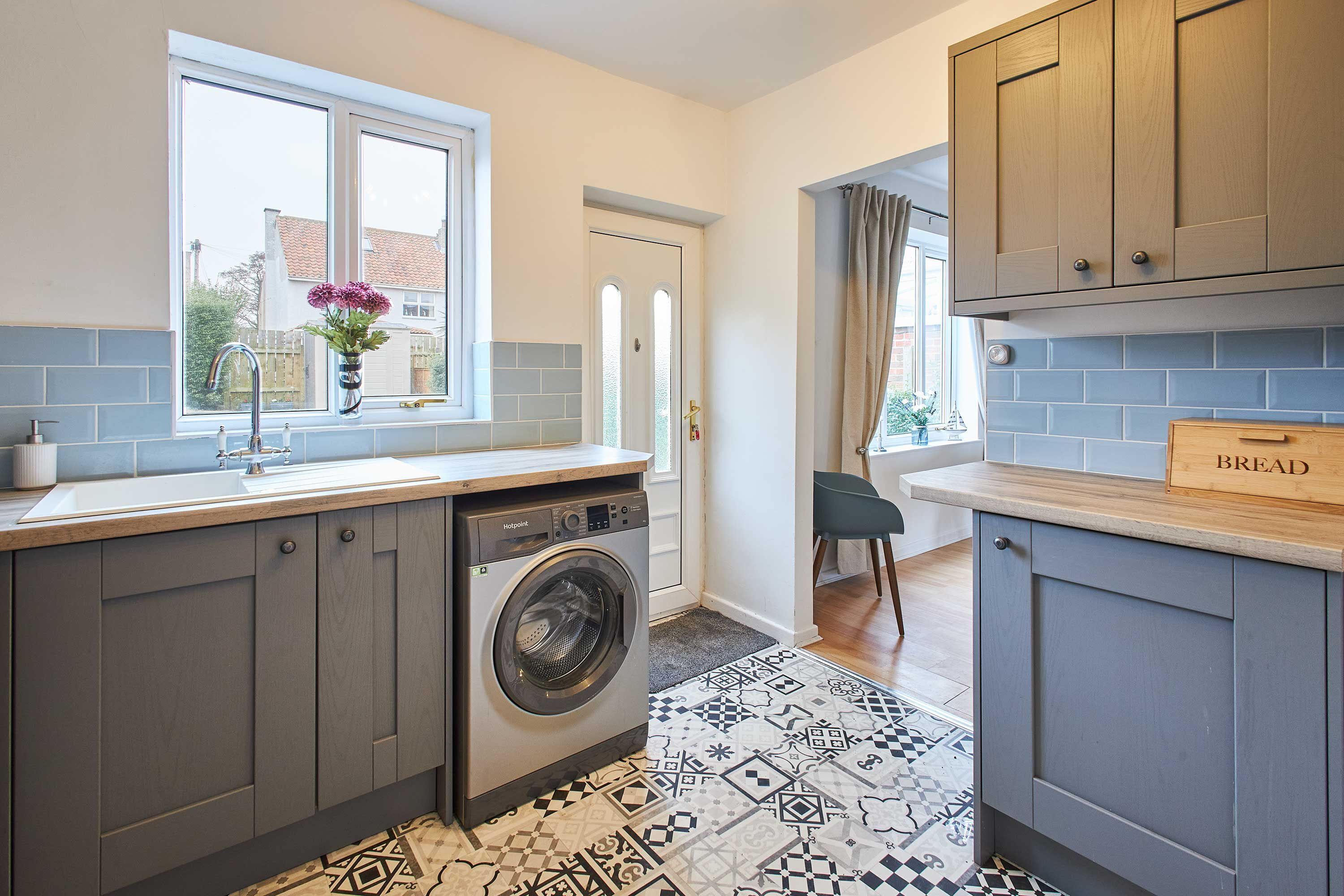 A kitchen with grey cabinets, a washing machine, a window with a view, and a patterned floor.