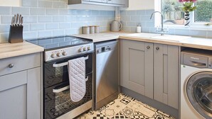 Una cocina compacta con armarios grises, horno integrado, lavadora y ventana con vistas a casas.